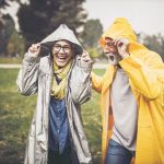 Happy senior couple in raincoats during rainy day in nature.