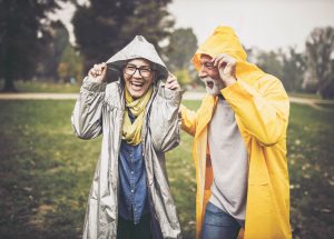 Happy senior couple in raincoats during rainy day in nature.