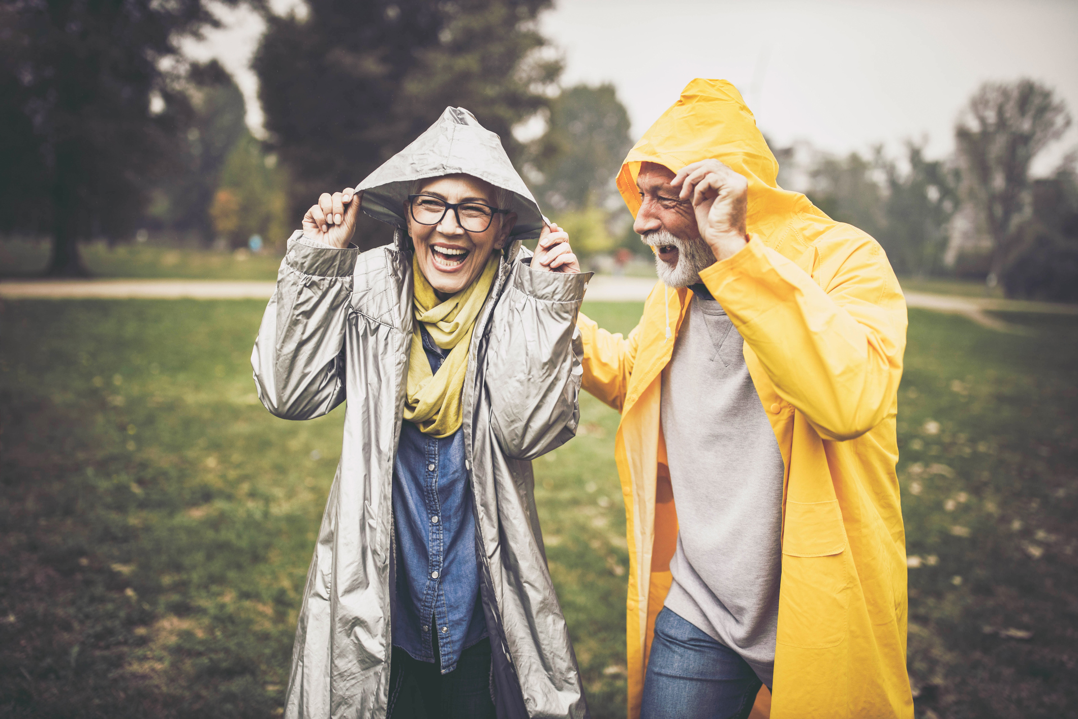 Happy senior couple in raincoats during rainy day in nature.